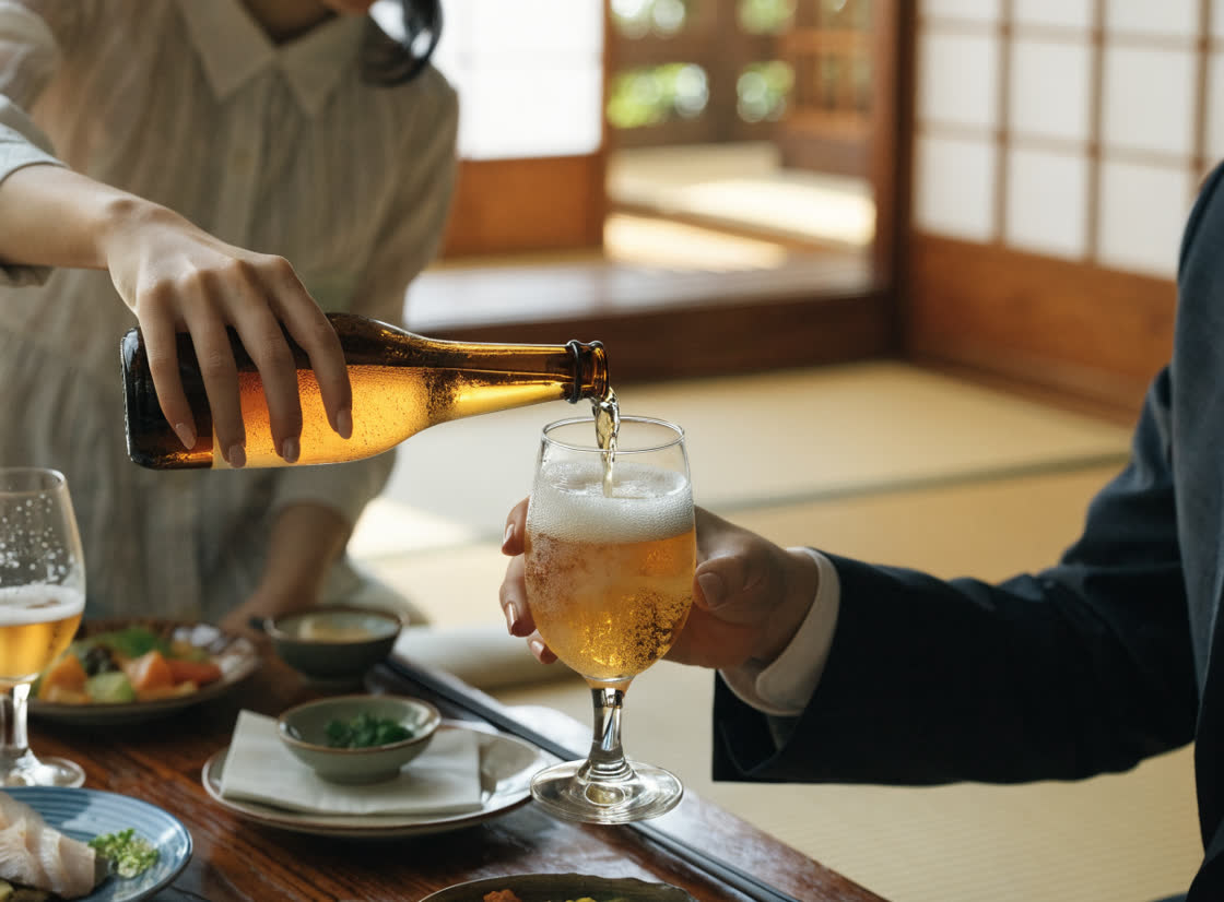 座敷の低いテーブルで、瓶ビールをグラスに注いでいる手元